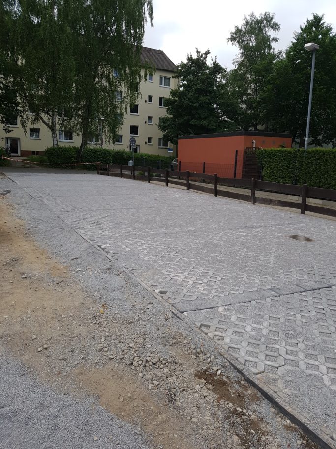 Gepflasterte Straße mit Gebäuden und Bäumen im Hintergrund.